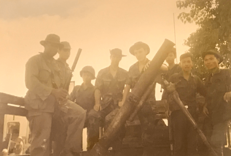 A group of U.S. soldiers gathered around a large piece of weaponry.
