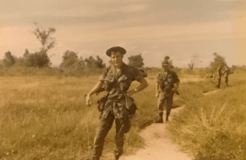 U.S. soldiers coming down a narrow dirt path through fields.