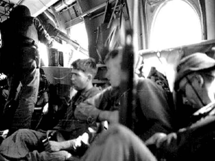 U.S. soldiers sitting in an aircraft, one standing at a mounted gun pointed out the window.