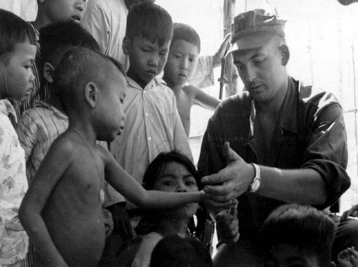 A U.S. soldier with a group of Asian children around him, showing them something in his hand.