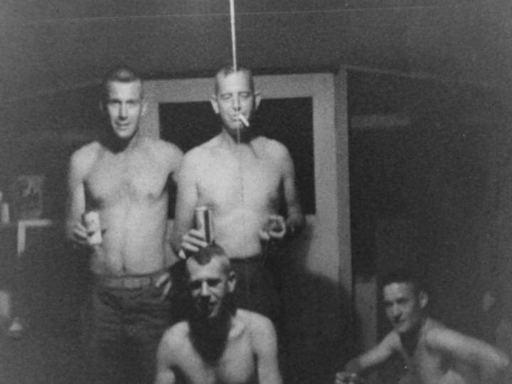 Four shirtless, young soldiers in their barracks at night, drinking beer and smoking cigarettes.