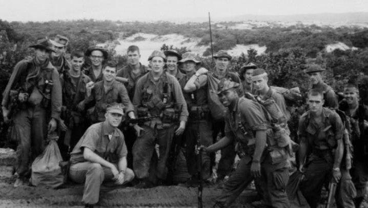 A group of about a dozen soldiers posed atop a mountain.