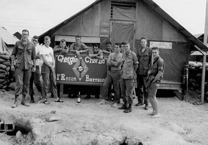 About a dozen soldiers posed around a sign that reads "Chargin Charlie, 1st Recon Battalion."