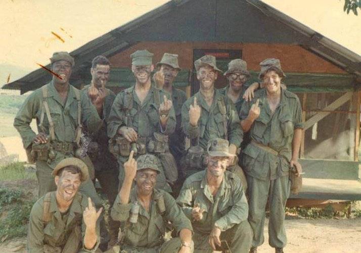 About a dozen U.S. soldiers with face paint on, posing for a photo with their middle fingers in the air.