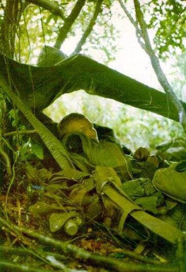 A soldier resting under a tarp in the jungle.