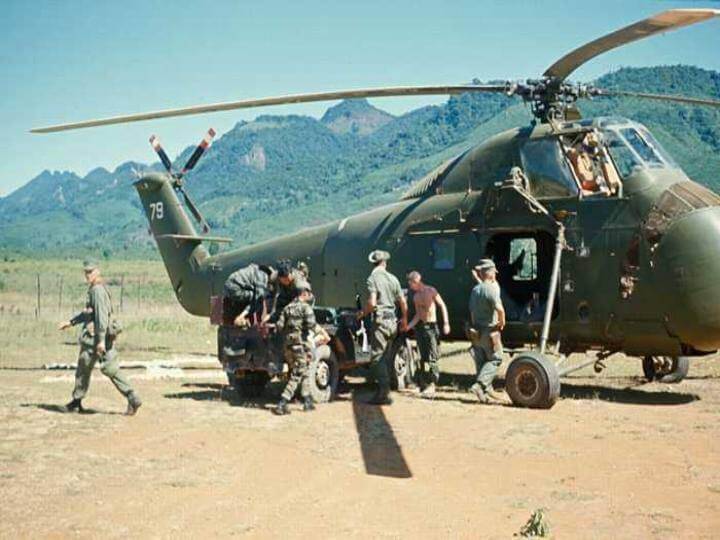 Soldiers loading up a helicopter, mountains in the background.
