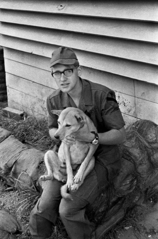 Young man in uniform, sitting outside and holding a medium sized dog on his lap.
