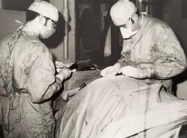 Two men in surgical gear working over a body.