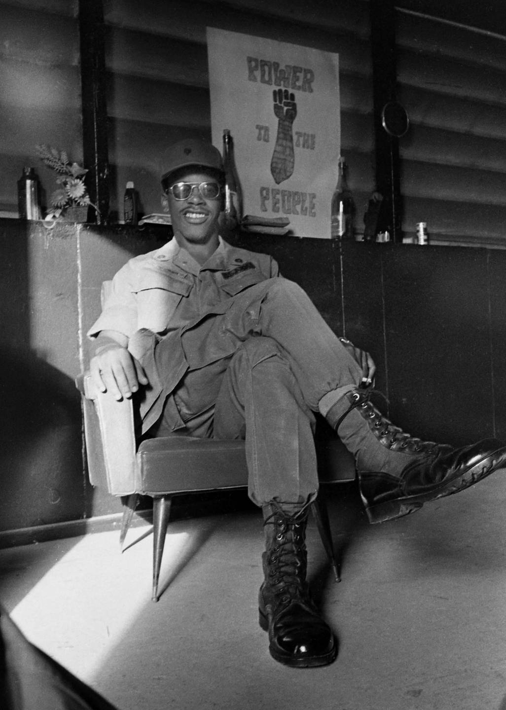 African-American soldier in a chair with a "power to the people" poster behind him.