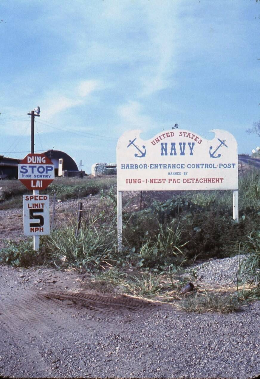 Signs on the side of the road: speed limit, stop sign, U.S. Navy Harbor-Entrance-Control-Post manned by IUWG-I-West-PAC-Detachment.