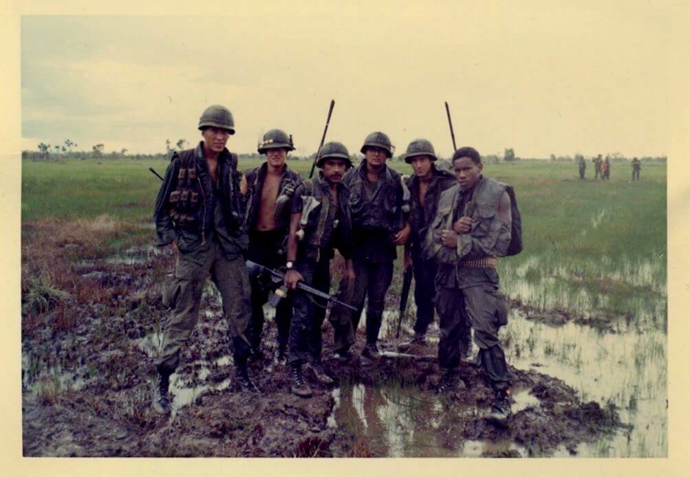 Six soldiers standing in muddy rice paddy fields.