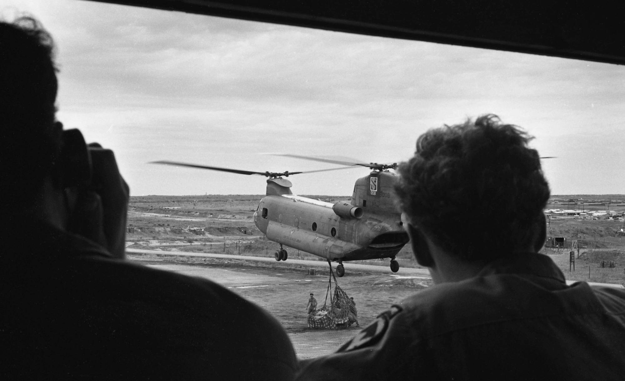 Soldiers watch a helicopter pick up cargo.