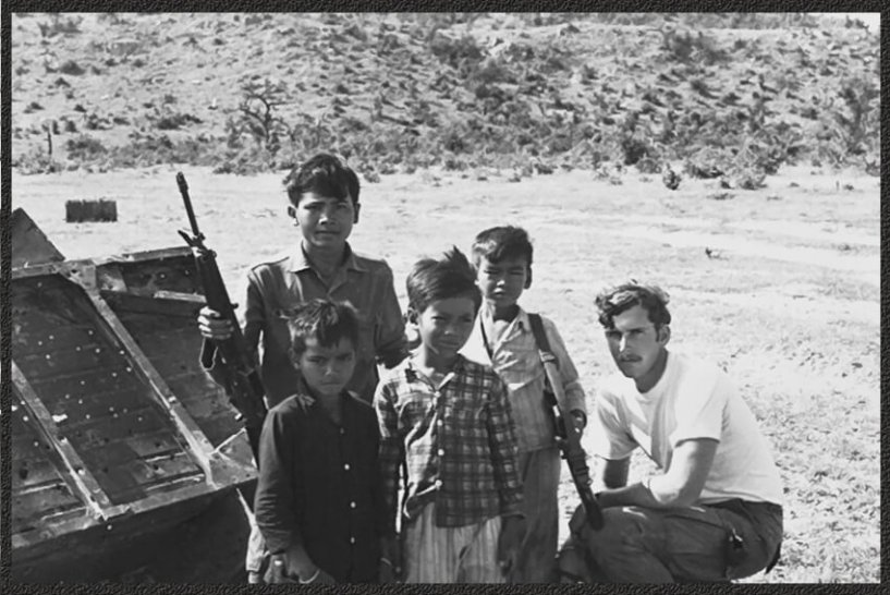 U.S. soldier with a group of young Asian boys, some holding rifles.