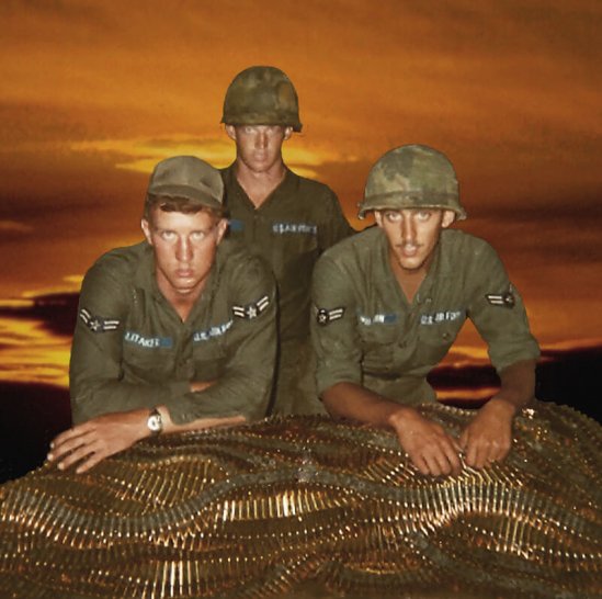 Three U.S. soldiers against an orange sky, leaning on piles of bandoliers.