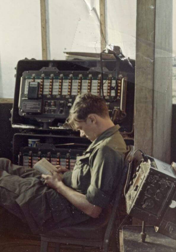 Young U.S. soldier relaxing and reading a book amid a bunch of technology.