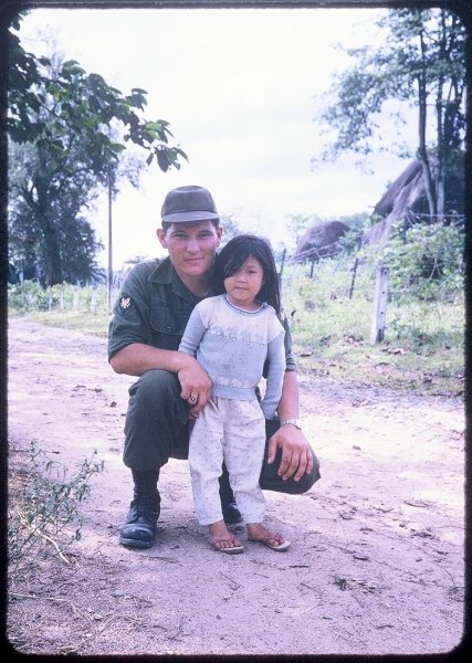 Young soldier crouched down beside a young Vietnamese girl.