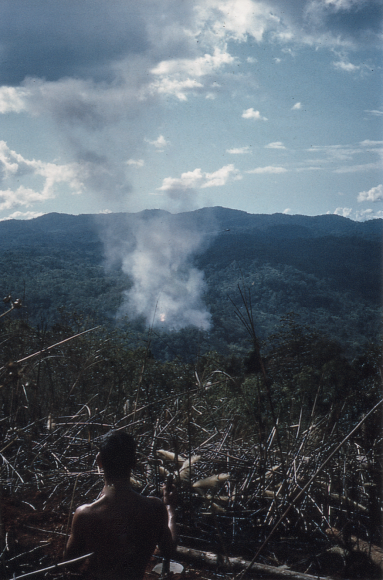 A young shirtless soldier on a mountain peak, looking over a smokey valley.