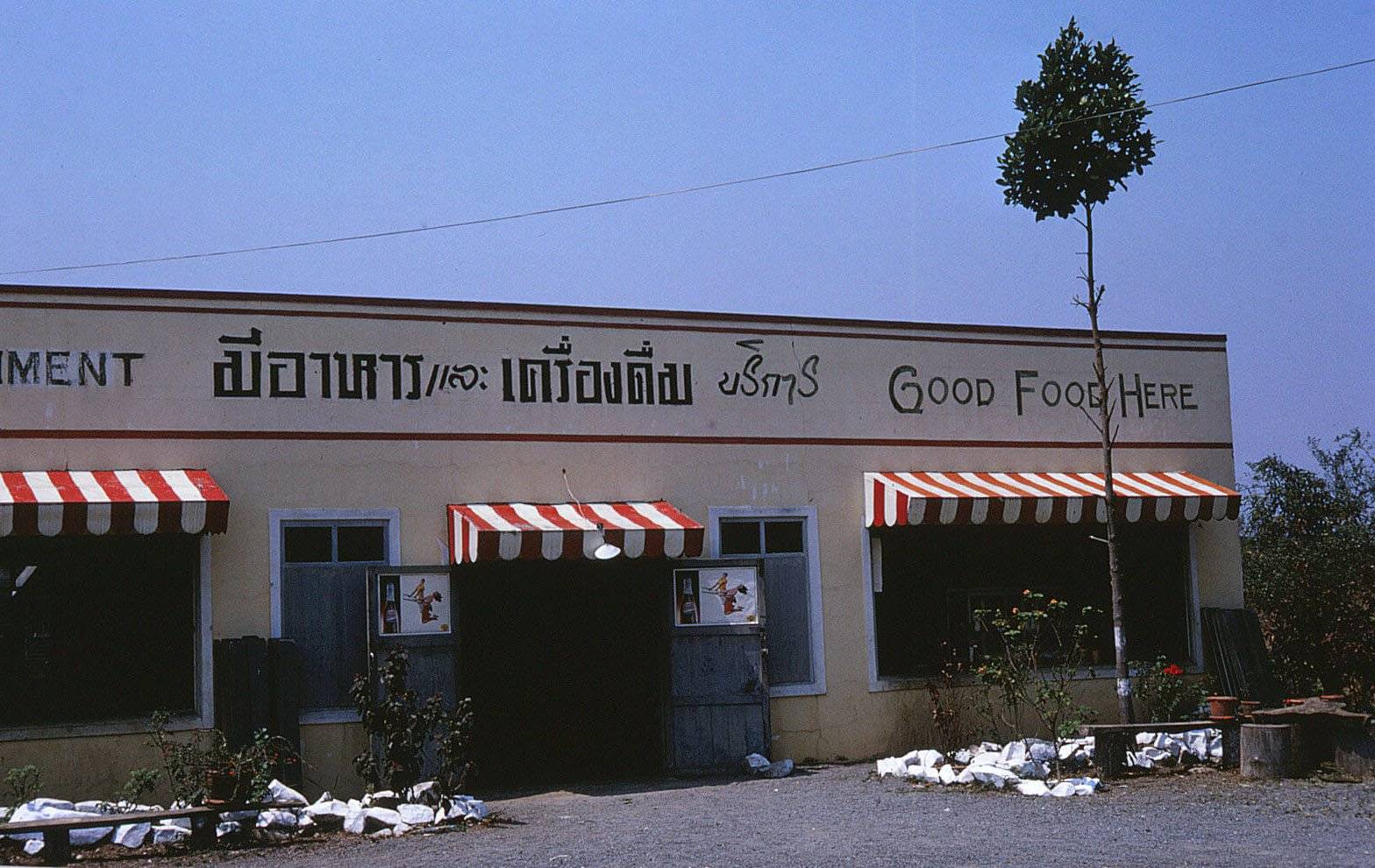 A one-story building against a blue sky. Writing on the building is in Asian language except for "Good Food Here."