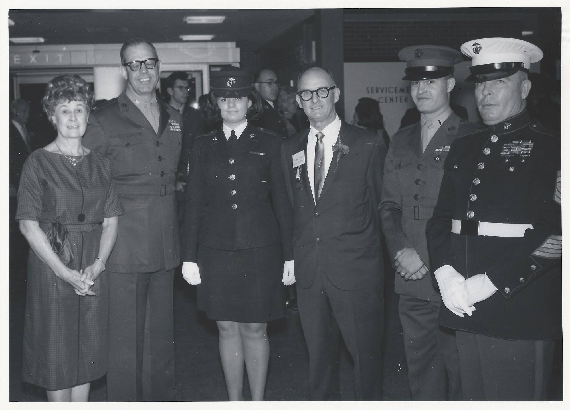 Servicemen and servicewoman and a civilian woman pose for a photo.