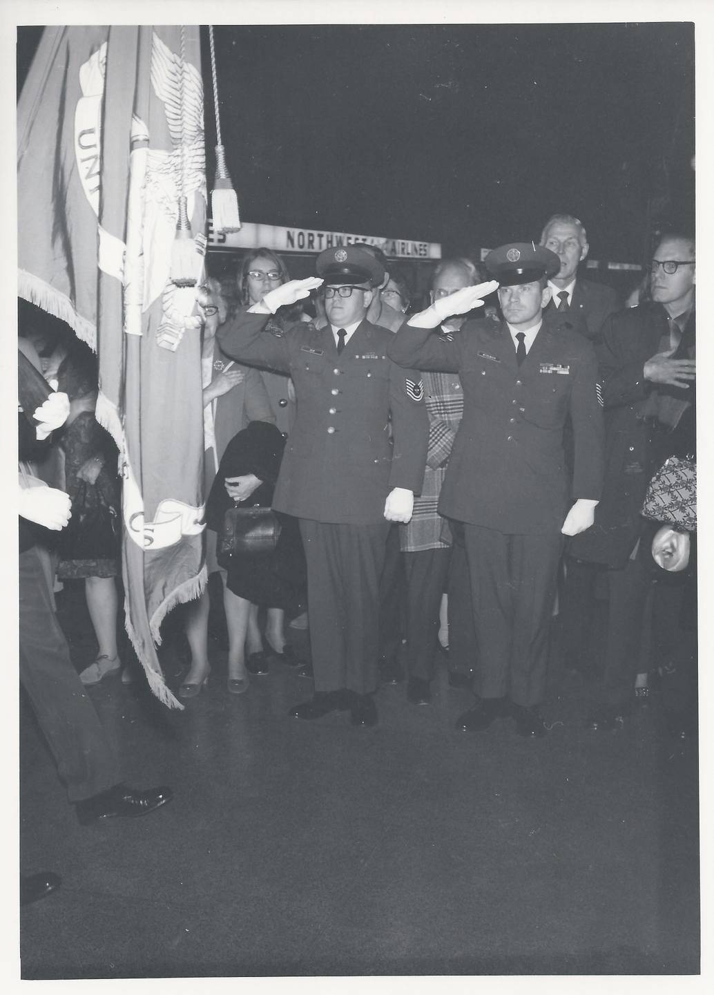 Two men in uniform saluting the flag while others watch.