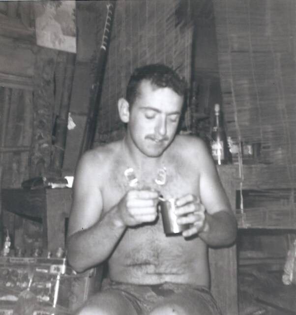 Young shirtless man inside his barracks, eating from a can.