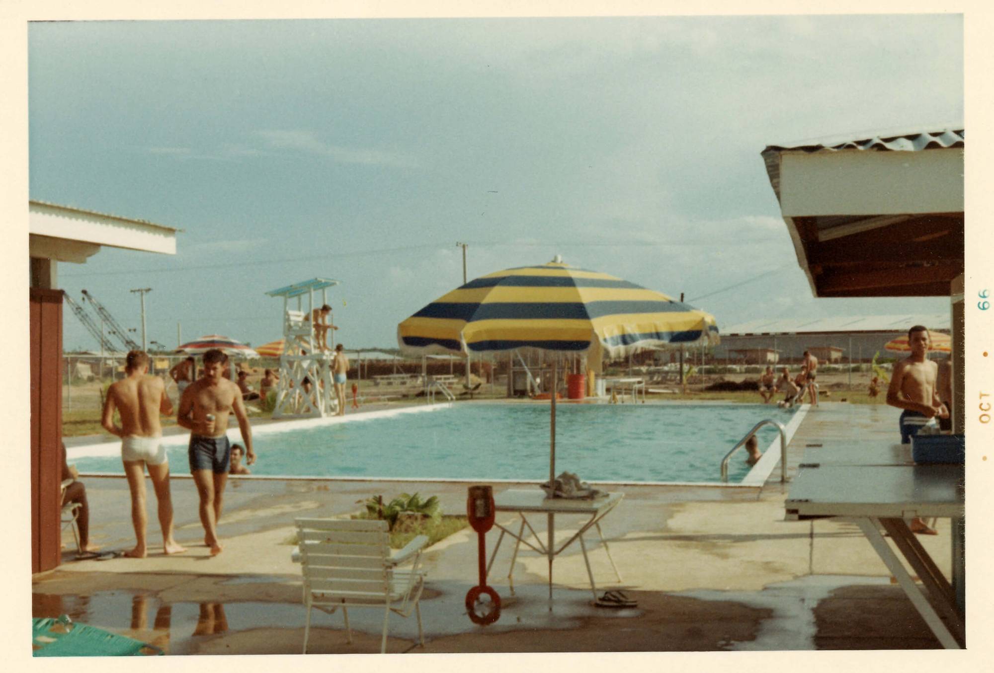 A swimming pool with a bunch of men in swimming shorts. Margins indicate the photo was taken October 1966.