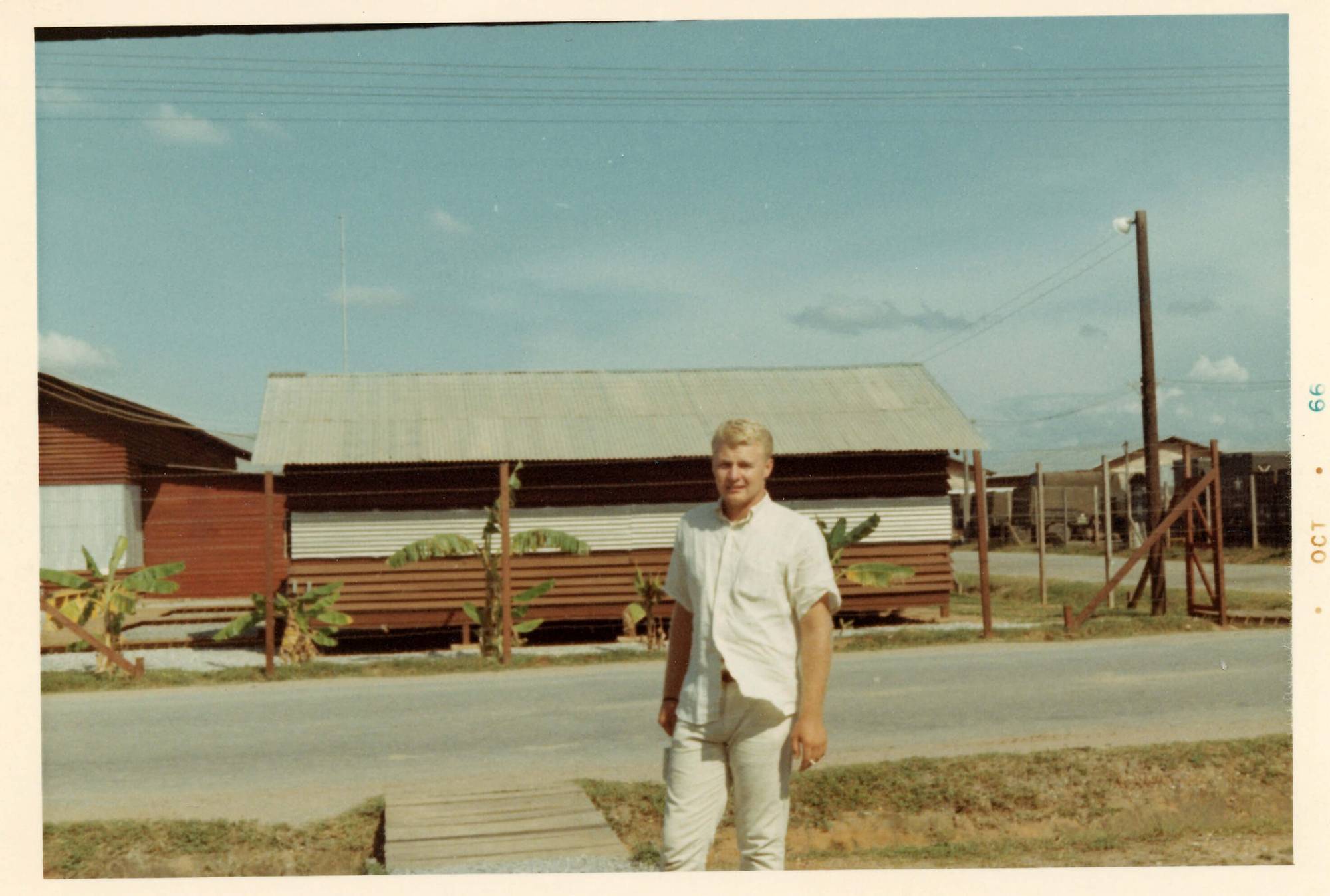 A young man dressed in white, standing outside a corrugated steel building. Margins indicate the photo is from October 1966.