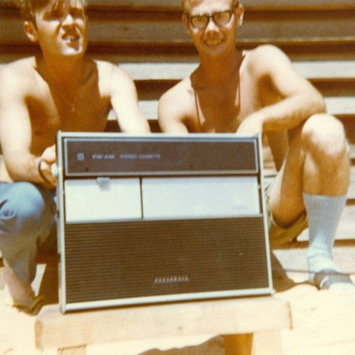 Two young men seated outside with a large radio.