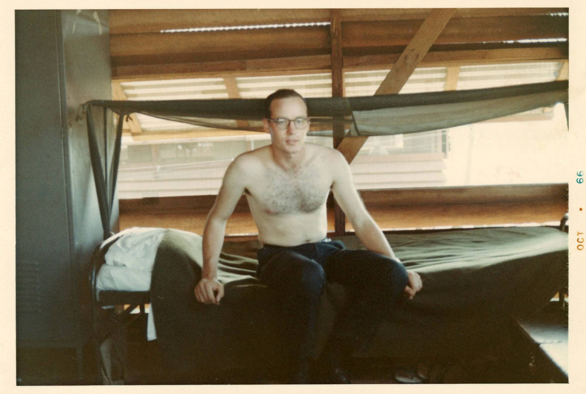 A shirtless young man wearing glasses, sitting on his bunk. Margins indicate photo is from October 1966.