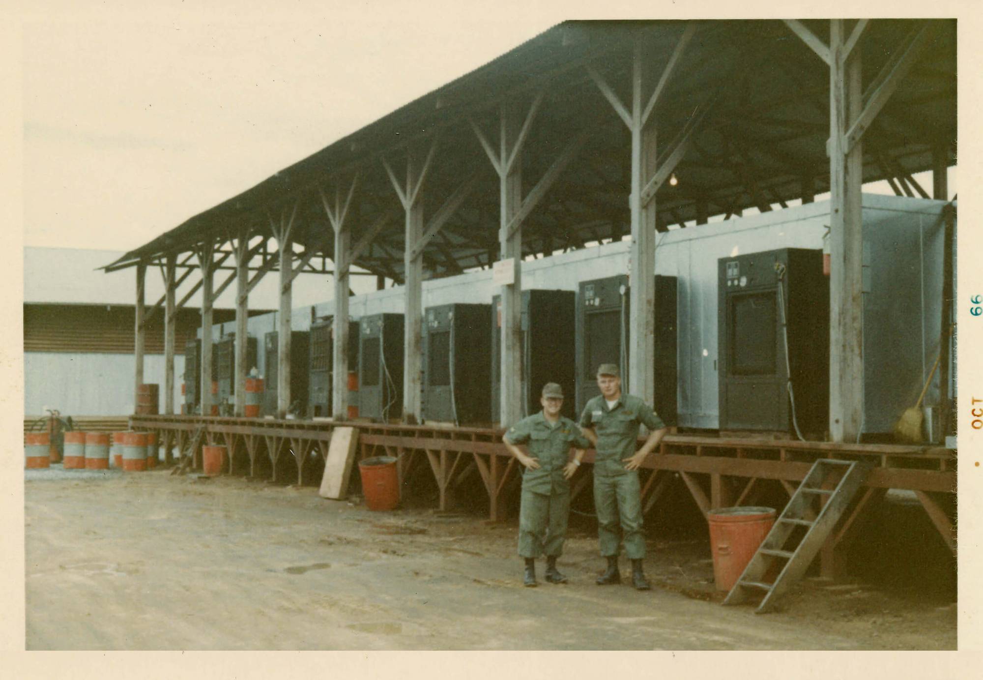 Two men in uniform posed with hands on hips, standing in front of a dock with many refrigerators on it.