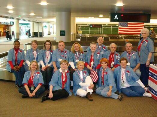 Contemporary photo of a group of people wearing red, white, and blue, seated near a luggage carousel.