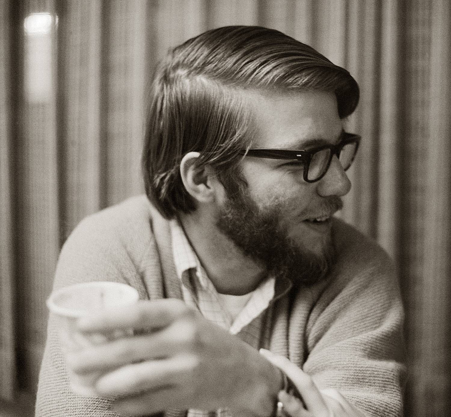 A young man with longer hear and glasses, dixie cup in hand, looking off camera to his left.