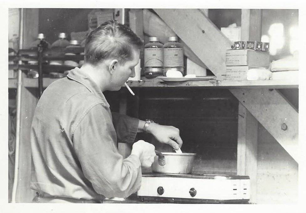 A young man cooking over a stove, cigarette in mouth.