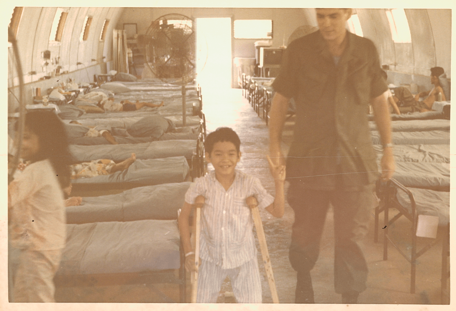 Young Asian patient on crutches, smiling, holding up a peace sign.