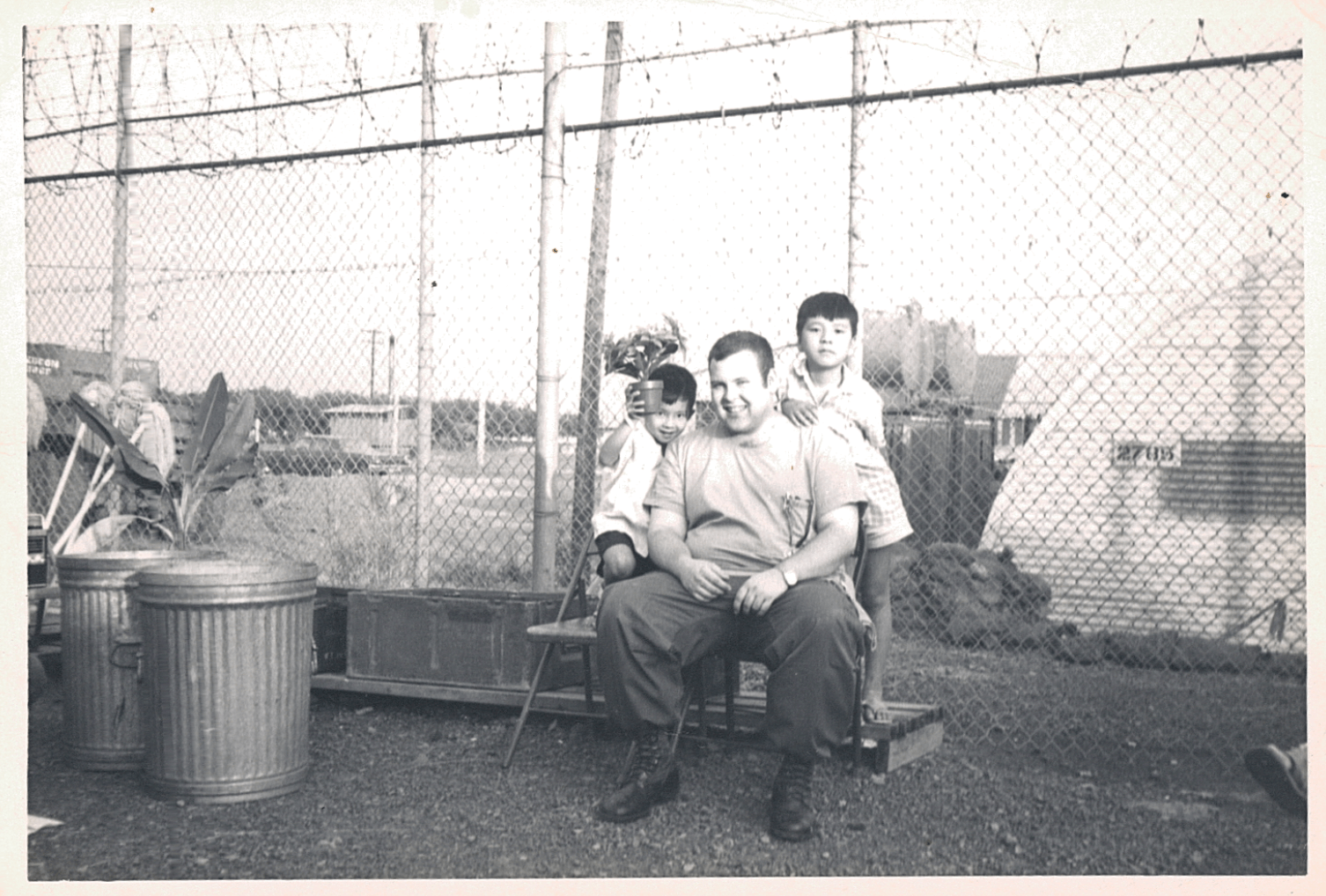 American soldier seated with two Asian children climbing on him.