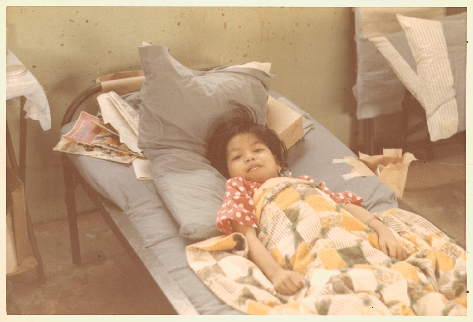 A young Asian child in her hospital bed, under a colorful quilt.