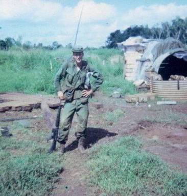 U.S. soldier in fatigues, standing next to a bunker outside the jungle.