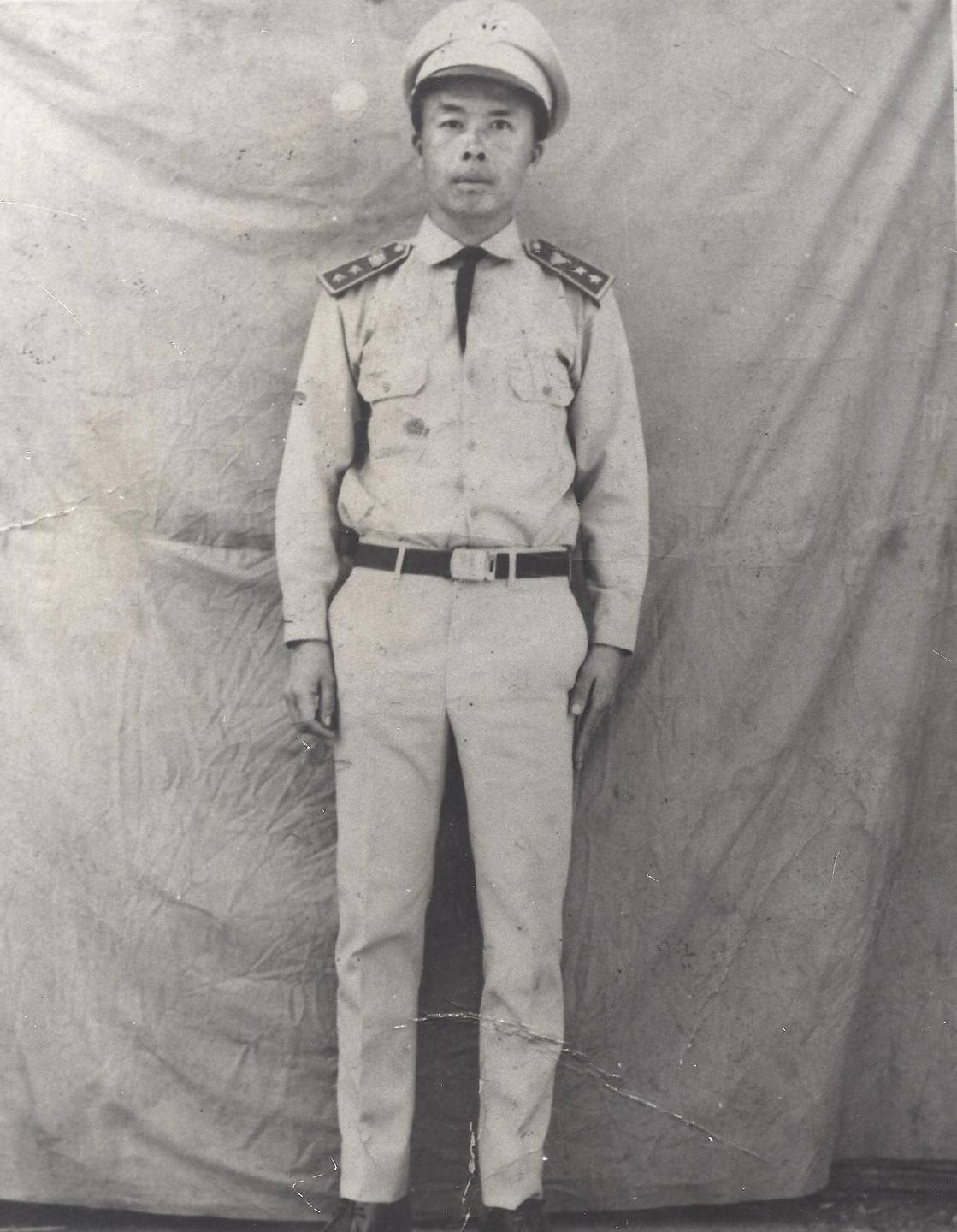 An Asian man in uniform standing against wrinkled canvas backdrop.