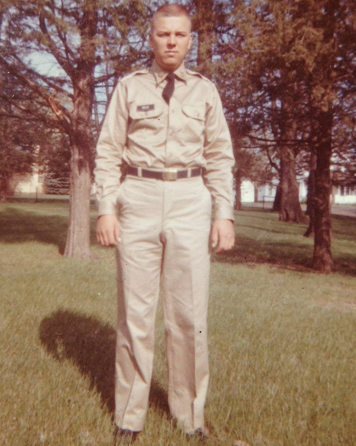 Young U.S. soldier in uniform, standing in a field of grass and trees.