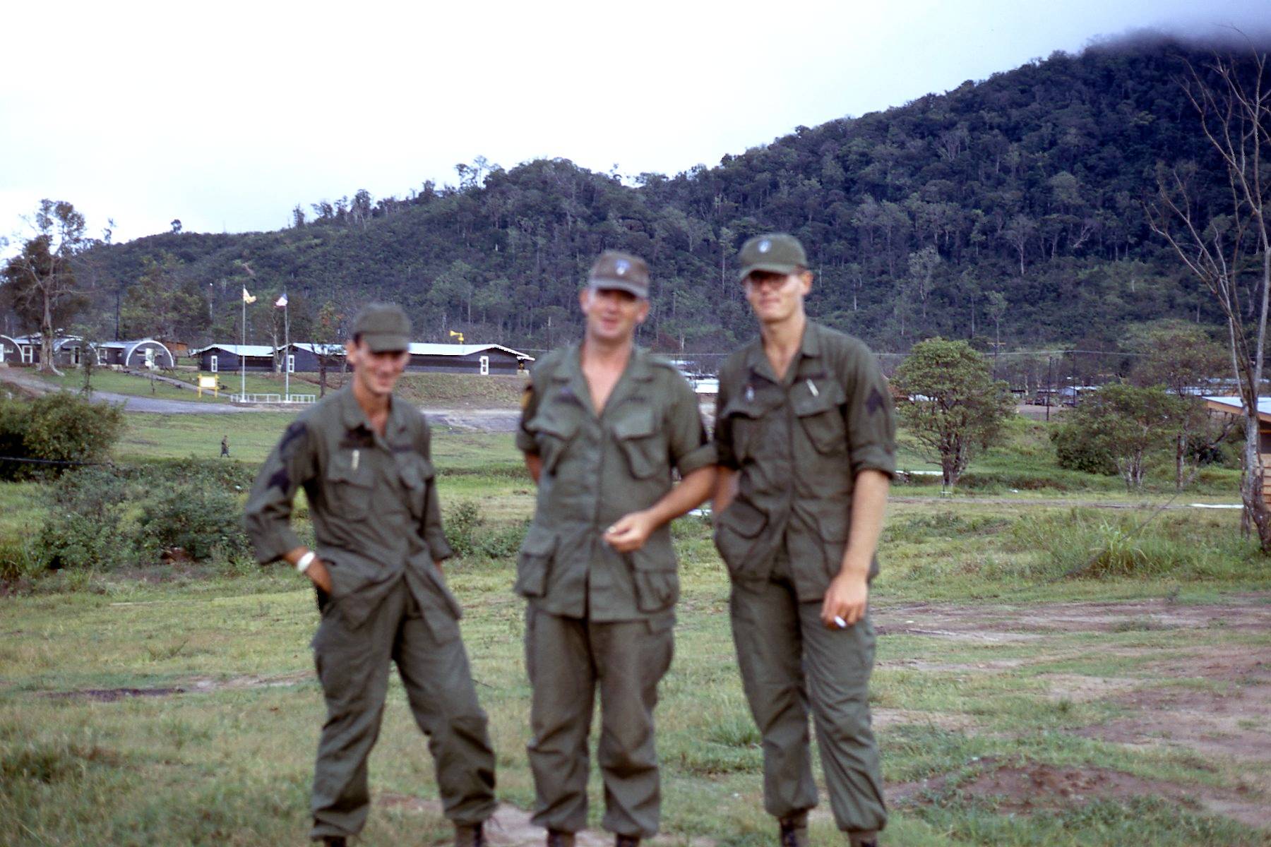 Three U.S. soldiers standing outside, mountains in the near background.
