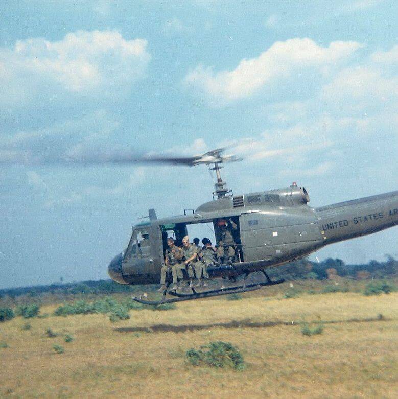 U.S. soldiers on a sitting out the side of a Huey helicopter in flight.