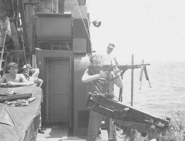 Soldier shooting a rifle off the deck of a ship.