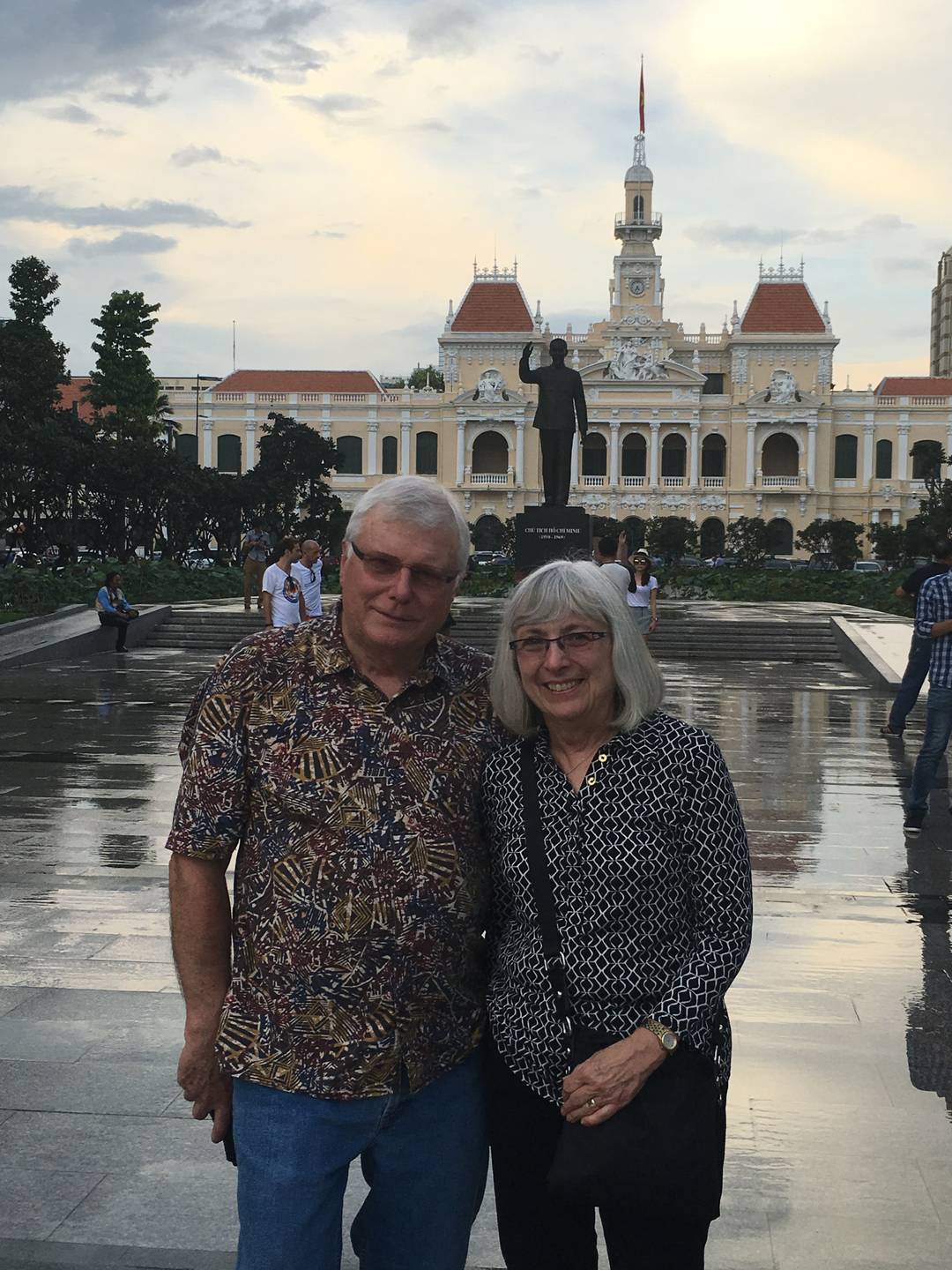 Modern photo of an older American couple standing in front of a monument in Saigon.