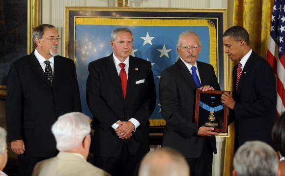 Contemporary photo of three men in suits and President Obama handing one of them a framed medal of honor.