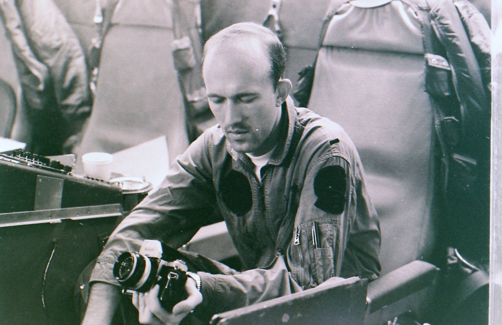 A man seated in what looks to be an aircraft, with a camera in his hand.