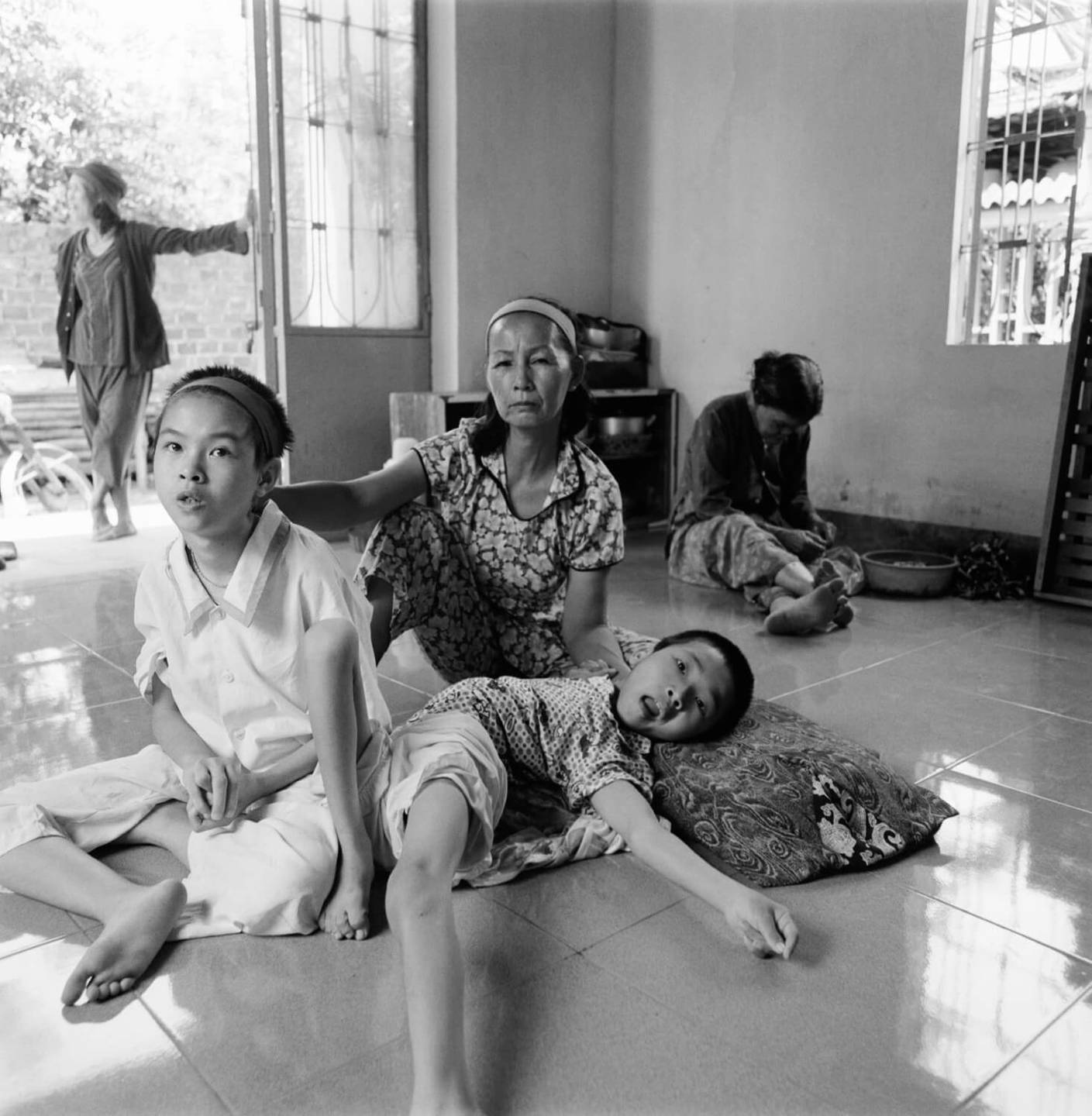 Asian family sitting on a tile floor. One child lays and his body is contorted.