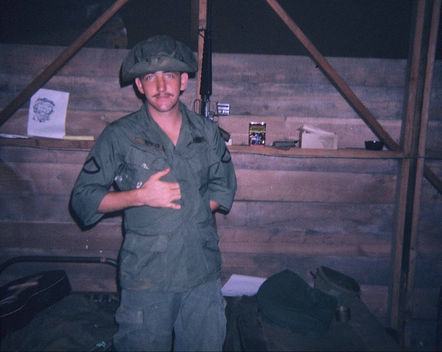 Young U.S. soldier at night in a boonie hat, inside a barracks.