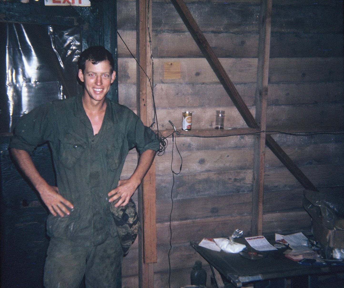 Young U.S. soldier in a barracks at night, smiling and with his hands on his hips.