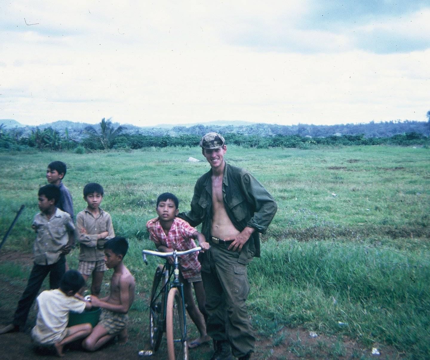 U.S. soldier in a verdant field with a group of Vietnamese children.