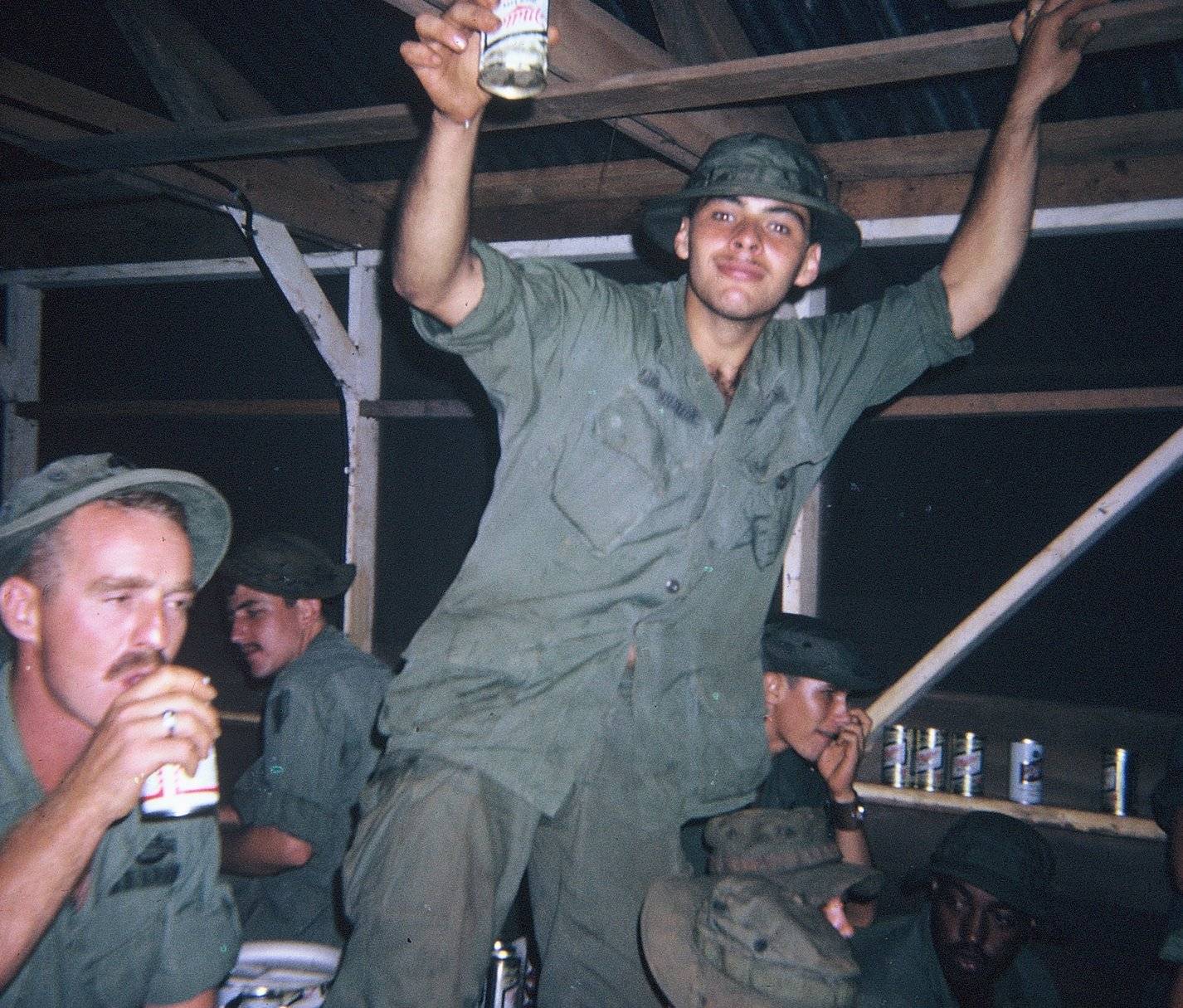 Group of soldiers drinking cans of beer at nighttime.